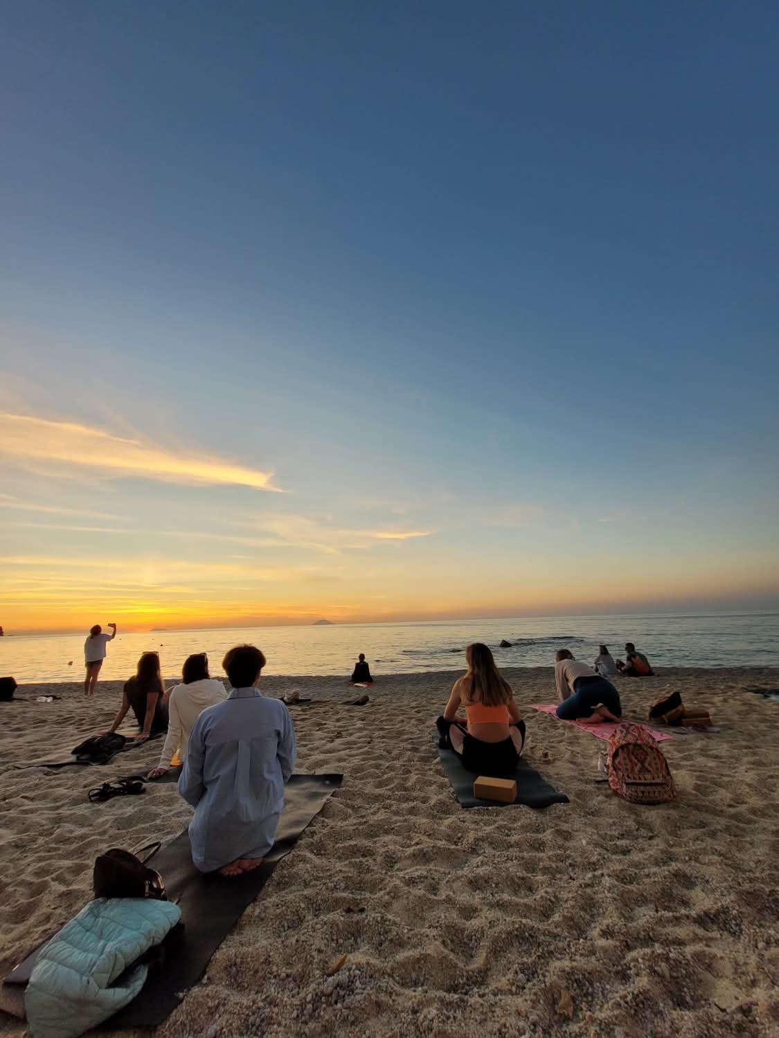 group doing yoga sitting by the sea